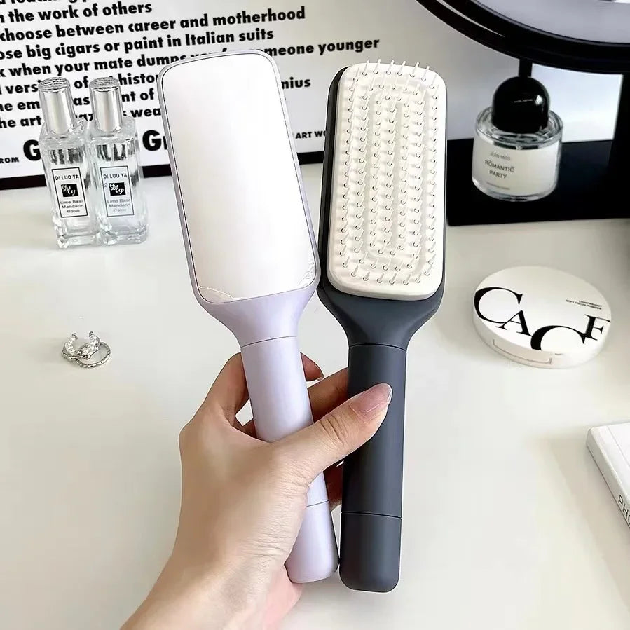 Hand holding white and black hairbrushes with cushioned bristles, ideal for detangling and styling hair at home.